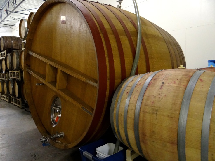 The large wooden vessel is called a foeder.  This one is full of fermenting beer as evidenced by the large hose coming out of the top.  The wine and spirit barrels visible in the background are used to age beer once the primary fermentation has finished.